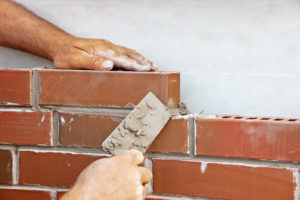 Mason bricklaying red bricks against a white wall